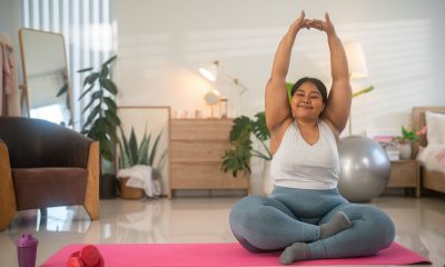 A smiling woman sitting on a yoga mat with arms stretched up over her head