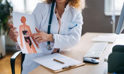 A doctor in a lab coat seated at her desk demonstrates the human digestive system on a chart in a modern medical office