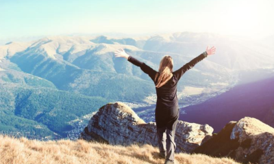 A woman standing on top of a mountain with arms outstretched in a victorious pose