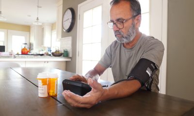 Man wearing glasses measures his blood pressure at kitchen table