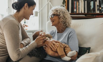 Grandmotherly woman holds baby while smiling at young mother