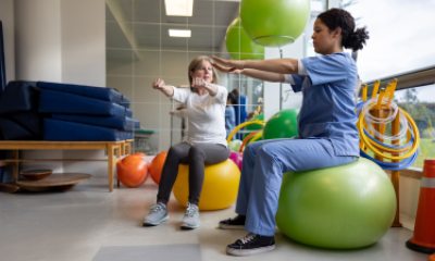 therapist uses balance ball to show exercise to a woman patient