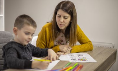 Young child draws on paper while sitting next to young woman