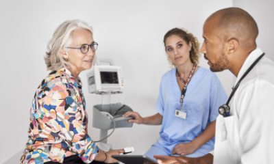 Woman with white hair sits on exam table and talks with nurse and doctor
