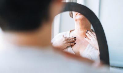 woman looks into mirror and touches front of neck