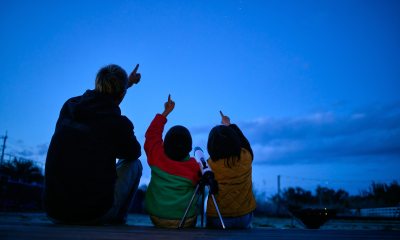 adult and two children sit outside and point at the darkening sky