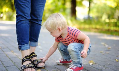 small child bends to touch the sandals of an adult in a parklike setting