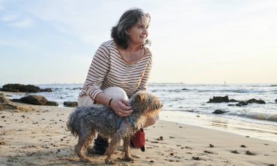 Woman crouches by her small dog on the beach