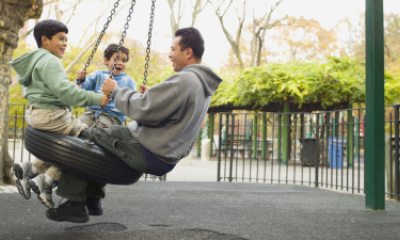 Dad and two young boys play on tire swing at park