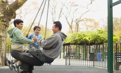 Dad and two young boys play on tire swing at park