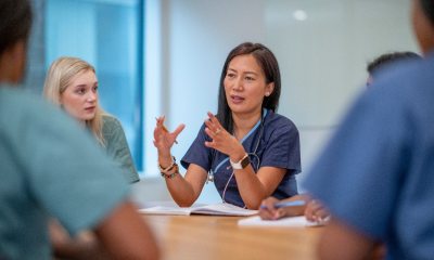 A woman caregiver sitting at a table and speaking at a meeting. Other caregivers are partially in frame but out of focus