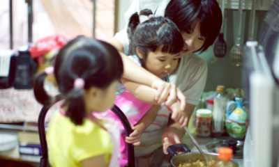 Young girls help adult fix soup in kitchen