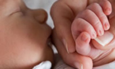 Close-up of adult hand holding a sleeping newborn baby's hand