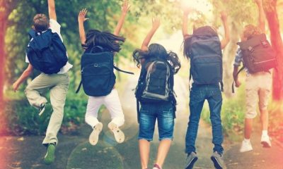 Kids wearing backpacks jump in the air in excitement