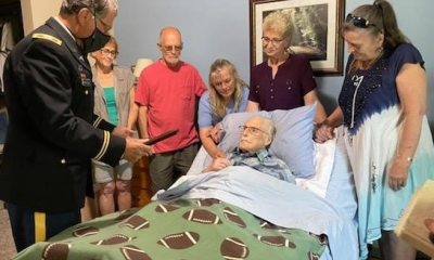 A Veteran being pinned with a medal while in a hospital bed, with family and friends around him.