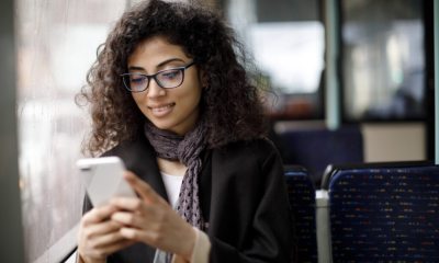 A young woman sitting on the bus or train, checking her mobile phone and smiling