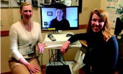 Two providers sit at a TeleHealth (TV Monitor) with a patient onscreen