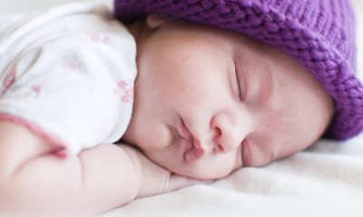A newborn in a purple knitted hat sleeping