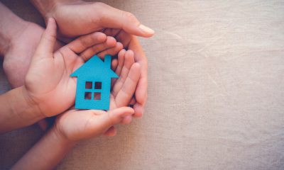 Two pairs of hands hold a cardboard cutout of a blue house