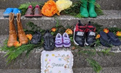 Shoes and flowers placed on a steps in remembrance, with a pillow that reads "Peace"