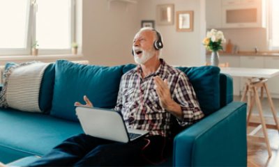 A man sitting on a couch with a laptop and headphones, singing or reacting jubilantly to the sound