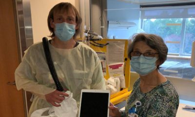 In masks, Chaplain Nettie and Andy Fisher display an Ipad in a patient room.