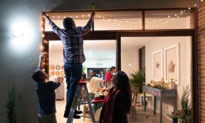 three people hang Christmas lights on house
