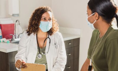 Doctor wearing a mask talks with a patient in exam room