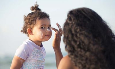 mom applies sunscreen to a toddler at the beach
