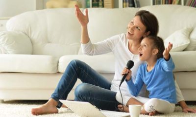 A mom and daughter sit next to a couch and sing karaoke together
