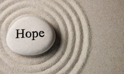 A stone with the word "Hope" rests in a sand filled area with concentric circles around it.
