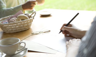 Close-up of hands writing a letter with glasses on the table