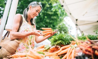 A smiling woman selects a bunch of carrots from a food stand