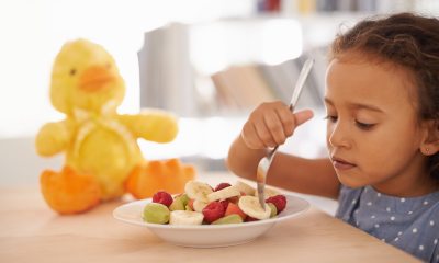 A child picking through fruit on a plate with their fork as a rubber duck sits in the background