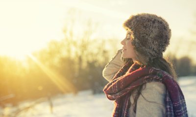 A woman in winter clothing on a field of snow feeling the warmth of the sun