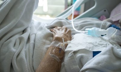 A patient with IV needles taped to their hand rests in a bed