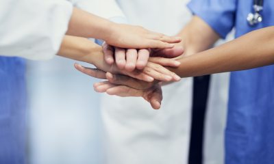 Health care providers in doctors jacket and scrubs stack hands