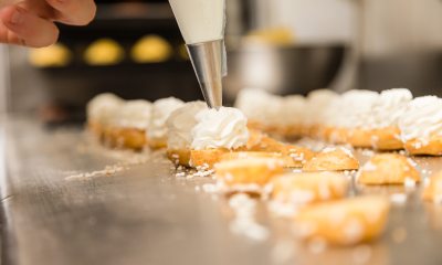 Close-up of baker's hand decorating pastries with whipped cream