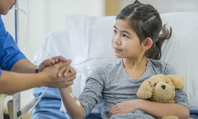 Young girl holding a teddy bear while resting in a patient bed