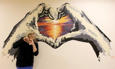 Lola Buckwald makes heart-hands next to her hand-themed mural