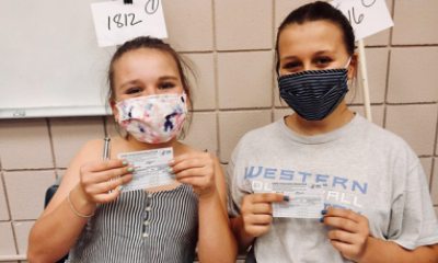 Roselli sisters smile behind masks as they hold their COVID-19 vaccine cards