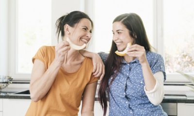 two women smile at each other as they enjoy fruit