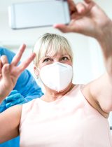 Woman holds up two fingers in a v as she receives vaccination and takes selfie