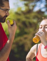 A runner eats and apple while another runner drinks juice