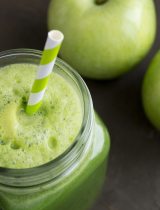 A green smoothie with a straw in a mason jar and green apples in the background