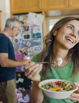 Middle aged woman happily eats a bowl of vegetables