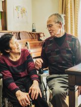 Woman in wheelchair smiles at older man sitting by a table