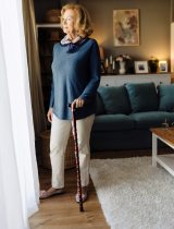Smiling woman stands near sunny door with help of a cane