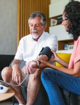 Older man having blood pressure checked by a woman with black hair