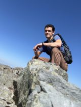 Justin crouching on a rock in front of a blue sky